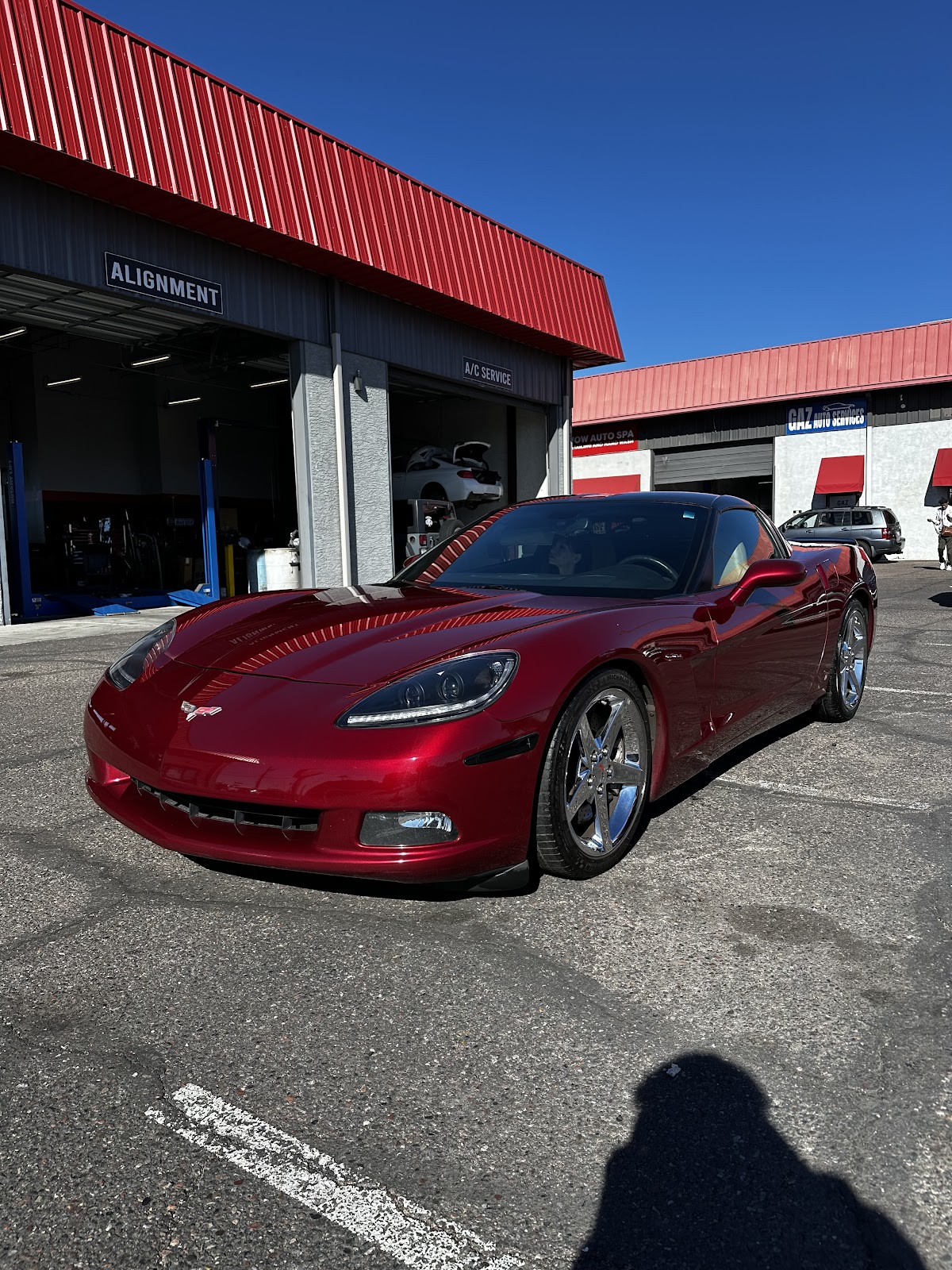 Deep red C6 Corvette parked in bright sun outside a row of service bays