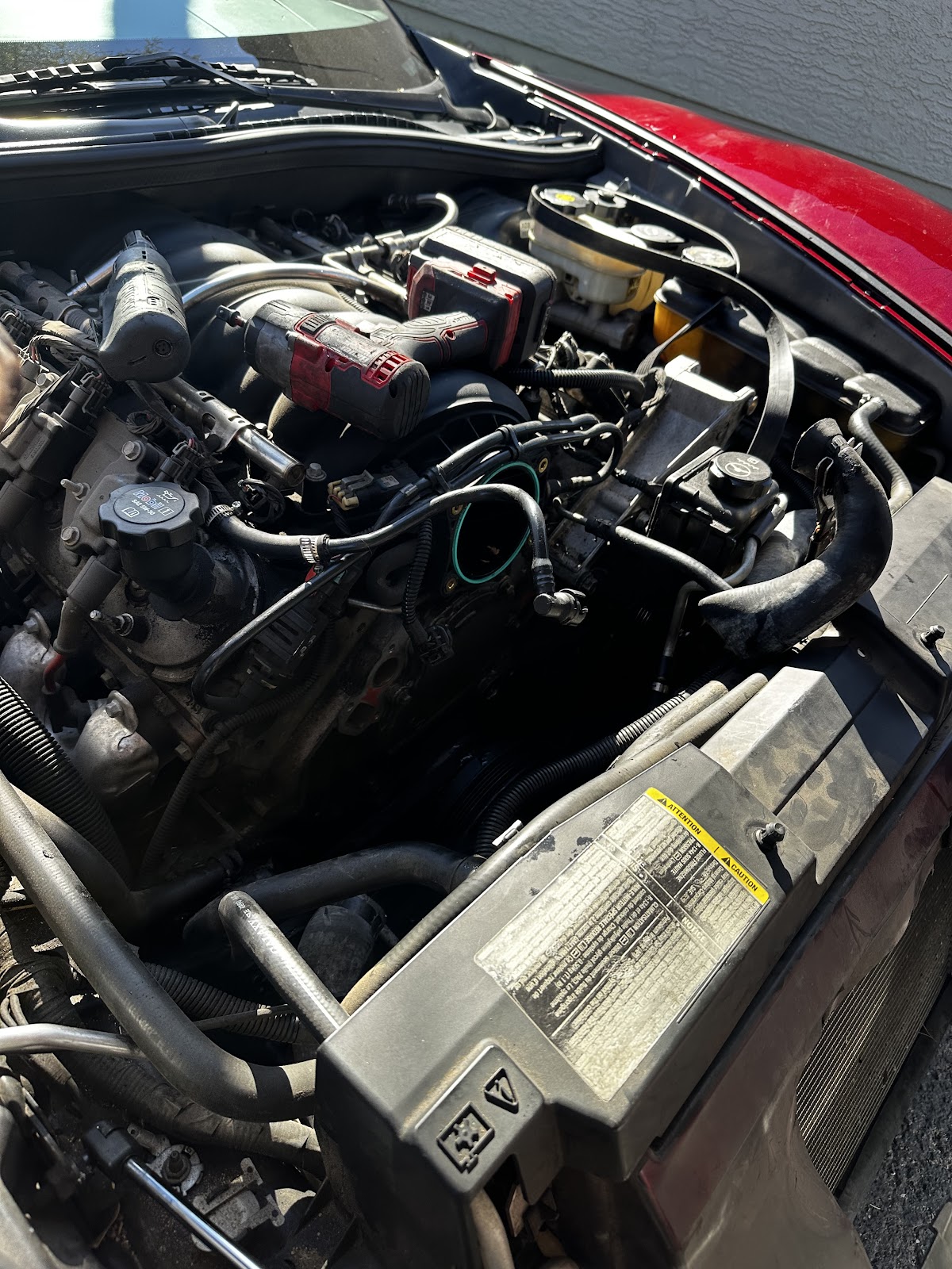 Engine bay of a red C6 Corvette with the throttle body removed and an impact driver resting on the intake