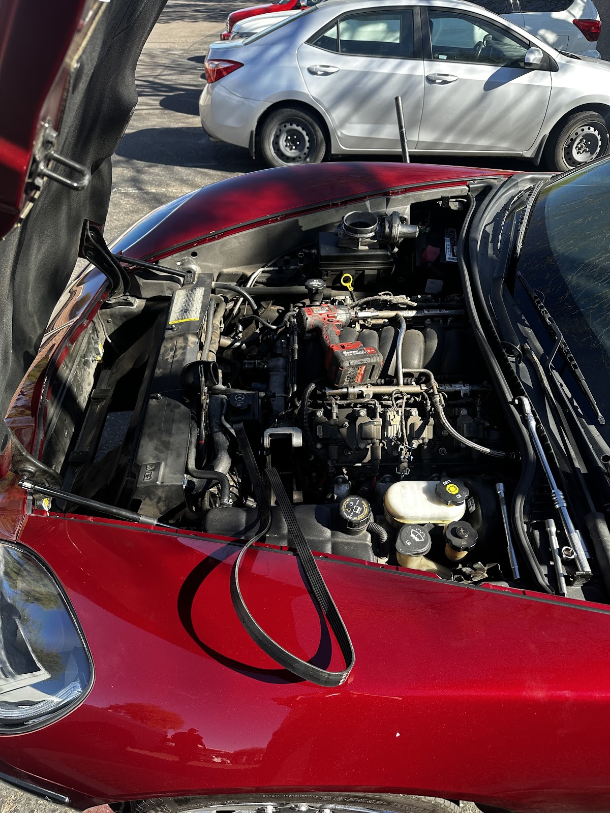Red Corvette with its hood open in a parking lot, serpentine belt draped over the fender